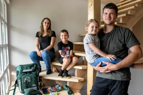 Familie auf Treppe, bereit für die Einschulung. Der Vater hält die Tochter, der Sohn sitzt daneben. Schulranzen und Mäppchen sind schon da.
