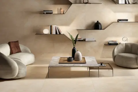Ein Wohnzimmer in warmen Beigetönen. Ein geschwungenes Sofa und ein Sessel laden zum Entspannen ein. Die Wandfliesen zeigen, wie die Farbe Beige aussieht.
