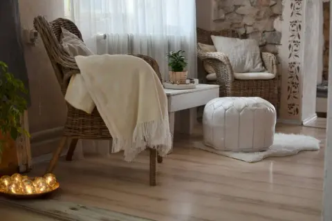 Gemütliches hygge style wohnzimmer mit Korbstühlen, weichen Decken und warmem Licht.
