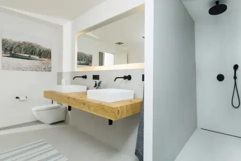 Modernes, fugenloses Bad mit Doppelwaschtisch auf Holzkonsole, wandhängendem WC und ebenerdiger Dusche. Ein Bild mit Boot und Schilf sorgt für maritime Akzente.