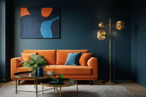 Ein orangefarbenes Sofa vor einer dunkelblauen Wand. Die Frage, welche Farbe passt zu blau Wandfarbe, wird hier mit einem kräftigen Orange beantwortet.