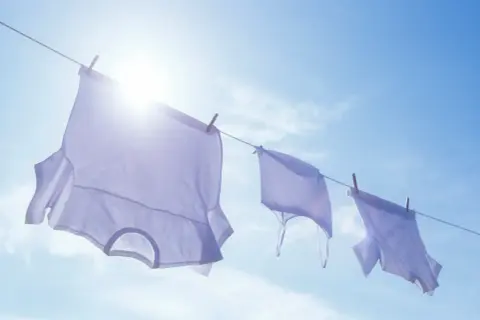 Drei weiße T-Shirts trocknen an einer Wäscheleine im Sonnenschein. Die Frage, wie oft man ein T-Shirt wechseln sollte, wird hier bildlich beantwortet: Wenn es frisch gewaschen ist!