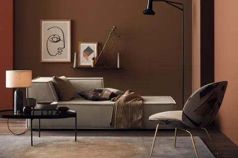 Gemütliches Wohnzimmer mit einer braunen Wand, einem hellen Sofa, einem auffälligen Sessel und einem Couchtisch.
