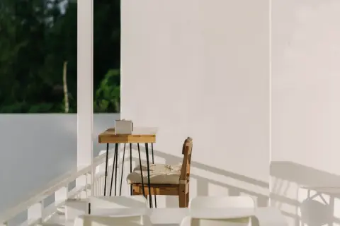 Ein Holztisch mit einer Box, ein Stuhl mit Kissen und weiße Möbel auf einer Terrasse. Hier lässt es sich schlicht und einfach leben.