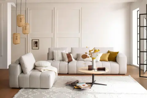 Gemütliches Wohnzimmer mit beiger Couch, Kissen, Couchtisch und Körblampen. Perfekt für slow living einrichtung.