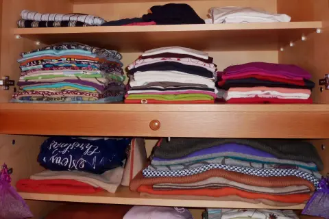 Ordentlich gestapelte Kleidung in einem Schrank. Zeit zum **Kleidung aussortieren** und Platz schaffen für Neues.