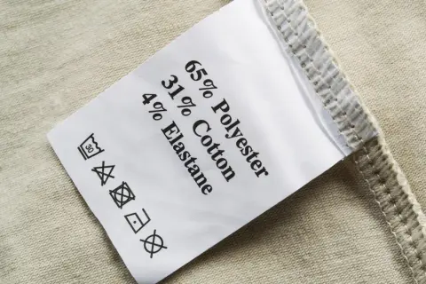 Pflegeetikett mit Materialzusammensetzung: 65% Polyester, 31% Baumwolle, 4% Elastan. Die Textilkette ist gut lesbar.