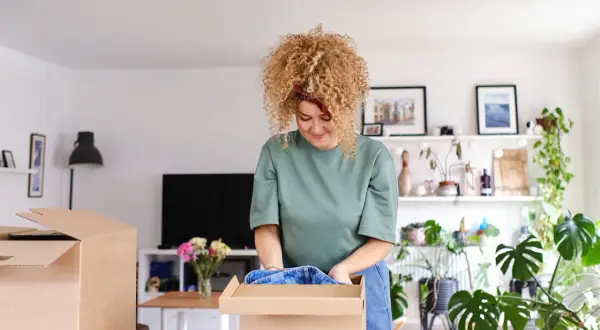Frau packt Kleidung in einen Karton. Sie sortiert ihre Sachen, vielleicht für den Verkauf von Flohmarktartikeln.