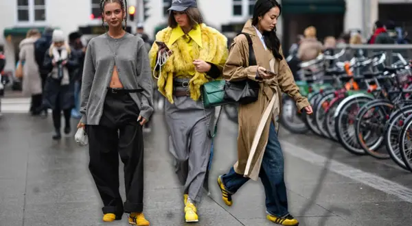 Drei Frauen in modischen Outfits, die die Herbstfarbe Gelb und Grau tragen, spazieren durch die Stadt.