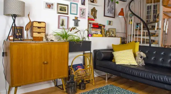 Gemütliche hygge einrichtung mit Vintage-Möbeln, Kunst und Pflanzen. Ein schwarzes Ledersofa lädt zum Entspannen ein.