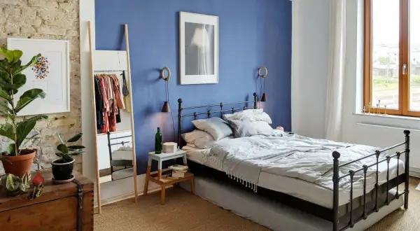 Gemütliches schlafzimmer blau grau mit Metallbett, Kleiderständer und Pflanzen.
