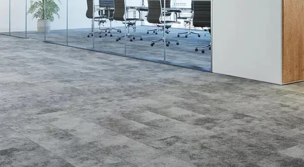 Moderner Teppichboden in Grau auf grauen Fliesen, der einen stilvollen Übergang zu einem Konferenzraum mit Glaswänden und Bürostühlen schafft.