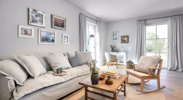 Gemütliches Wohnzimmer mit einem großen Sofa, einem Holztisch und einem Schaukelstuhl. Die warmes grau farbpalette schafft eine beruhigende Atmosphäre.