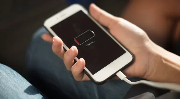 Hand hält Smartphone mit leerem Akku, das gerade geladen wird. Die Frage "wie lange handy nutzen" stellt sich, wenn der Akku fast leer ist.