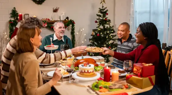 Familie feiert Weihnachten minimalistisch am festlich gedeckten Tisch. Ein Weihnachtsbaum und Kerzen sorgen für stimmungsvolles Licht.