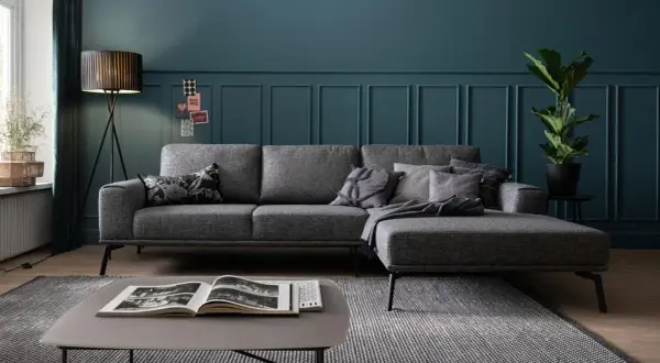Gemütliche graue Couch mit vielen Kissen auf einem gemusterten Teppich. Ein moderner Couchtisch mit Buch steht davor.