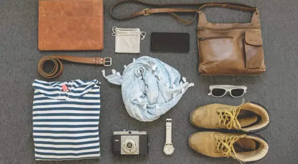 Minimalismus reisen: Ledermappe, gestreiftes Shirt, Schal, Kamera, Uhr, Tasche, Schuhe, Sonnenbrille.
