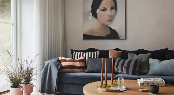 Gemütliches, warmes Wohnzimmer mit einem Sofa voller Kissen, einem Gemälde und einem Holztisch mit Kerzen.