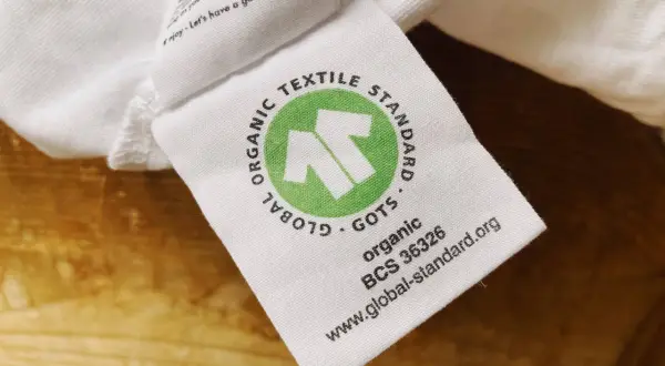 GOTS-zertifiziertes Textiletikett auf weißem Stoff. Die Kritik an der Textilindustrie wird durch das Siegel "Global Organic Textile Standard" entkräftet.