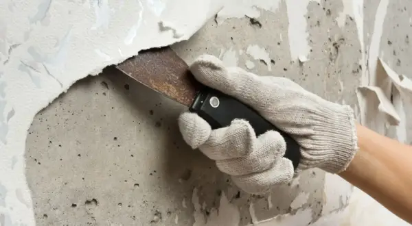 Mit einem Spachtel wird eine alte Tapete von der Wand entfernt. Die Arbeit, um die Fototapete zu entfernen, ist mühsam.