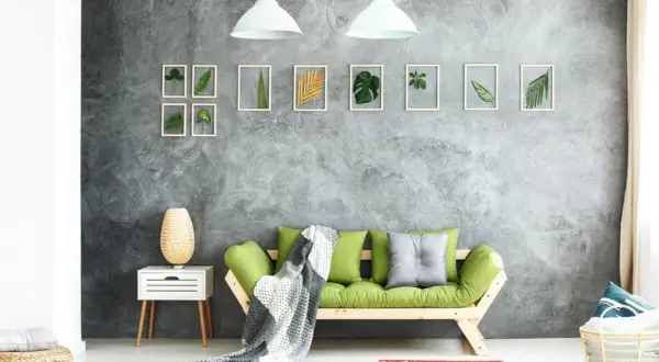 Graue Beton-Struktur Wand mit gerahmten Blättern und einem grünen Sofa.