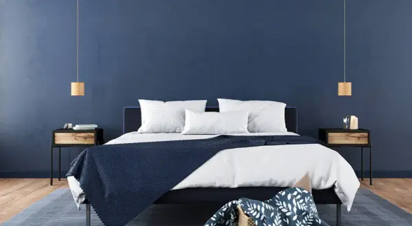 Ein modernes Schlafzimmer mit tiefblauen Wänden, die zum Streichen in Blau einladen. Ein dunkles Bett mit weißen Kissen und einer blauen Decke.