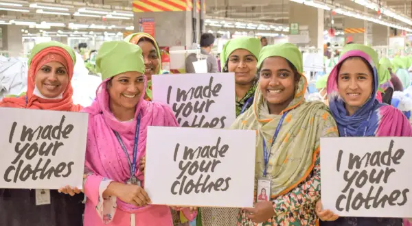 Frauen in einer Fabrik halten Schilder mit "I made your clothes". Dies unterstreicht die Bedeutung der Fair Wear Foundation für faire Arbeitsbedingungen.