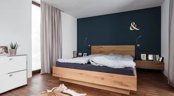 Modernes schlafzimmer blau holz mit einem Doppelbett aus hellem Holz, dunkler Wand und Teppich.