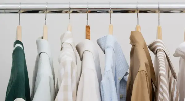 Eine Auswahl an Hemden und einem grünen Pullover für einen stilvollen **capsule wardrobe mann**.