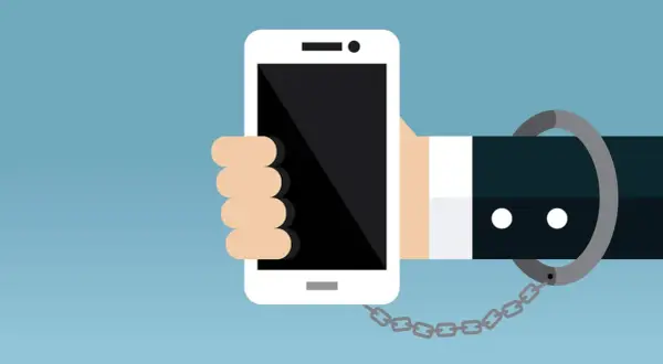 Eine Hand hält ein Smartphone, das mit einer Handschelle und Kette gefesselt ist. Ein Symbol für zu viel Handy-Nutzung.