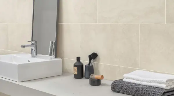 Sandfarbene Badezimmer Fliesen mit natürlicher Maserung, inspiriert von Stein. Ein moderner Waschtisch mit Armatur und Pflegeprodukten.