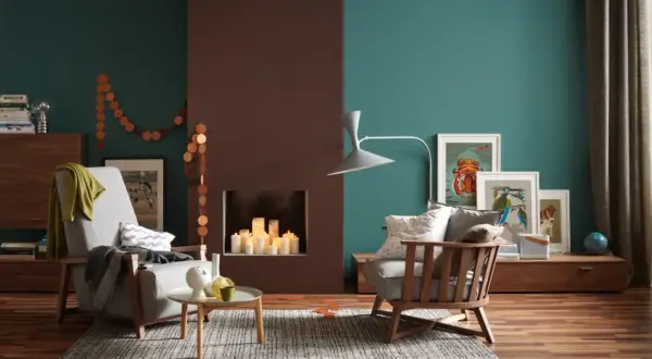 Gemütliches Wohnzimmer mit Kamin, Kerzen und Kunstwerken an den Wänden. Die Wandfarben in Petrol und Braun sind beliebte Wandfarben für ein warmes Ambiente.