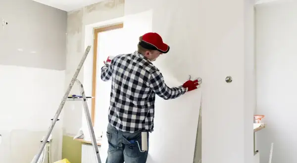 Mann mit roter Kappe tapeziert Wand. Verschiedene Raufasertapeten Arten sind für Renovierungen beliebt.