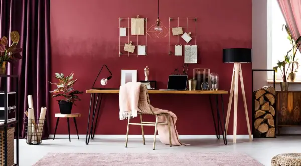 Ein modernes Arbeitszimmer mit einem Schreibtisch, Laptop und einer rosa Decke. Die rosa Wandfarbe wirkt warm und einladend.