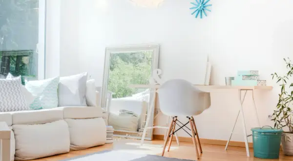 Ein helles, aufgeräumtes Wohnzimmer mit weißem Sofa, Spiegel und Schreibtisch. Perfekt, um das **Zimmer auszumisten** und Ordnung zu schaffen.