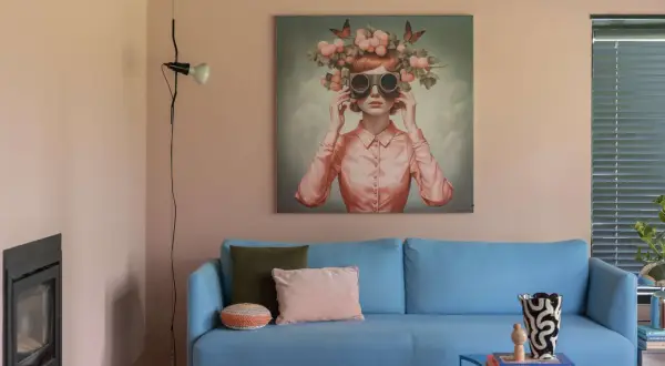 Sanfte Wandfarben im Wohnzimmer harmonieren mit einem blauen Sofa und einem surrealen Kunstwerk.