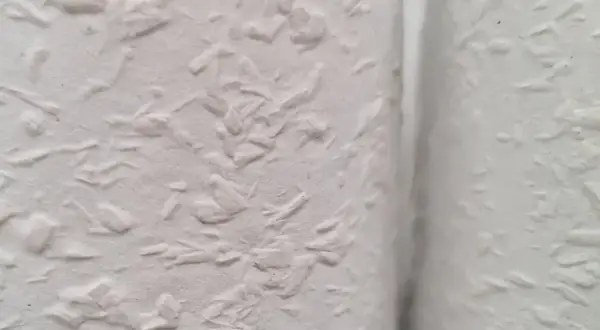 Nahaufnahme einer weißen Wand mit Raufaserputz innen. Die Struktur ist unregelmäßig und rustikal, perfekt für ein gemütliches Zuhause.