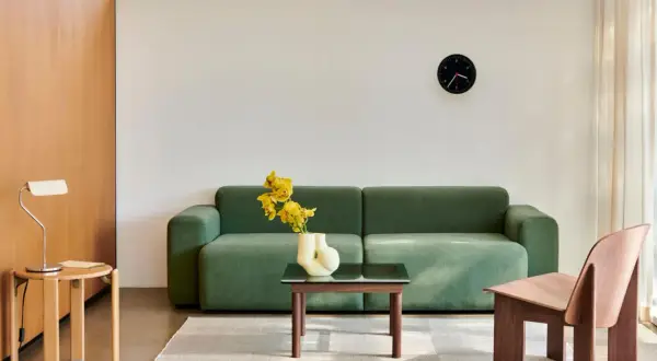 Ein Wohnzimmer im **Scandi Style** mit einem grünen Sofa, einem Holzsessel, einem Beistelltisch mit Lampe und einem Couchtisch mit gelben Blumen.