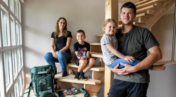 Familie auf Treppe, bereit für die Einschulung. Der Vater hält die Tochter, der Sohn sitzt daneben. Schulranzen und Mäppchen sind schon da.