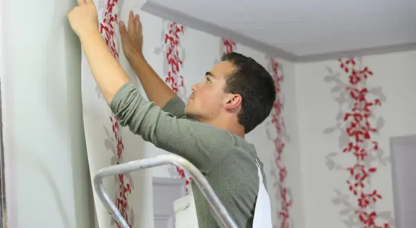 Mann bringt fototapete auf raufaser an. Rote Blumenmuster zieren die Wand.