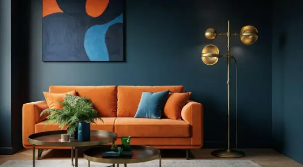 Ein orangefarbenes Sofa vor einer dunkelblauen Wand. Die Frage, welche Farbe passt zu blau Wandfarbe, wird hier mit einem kräftigen Orange beantwortet.