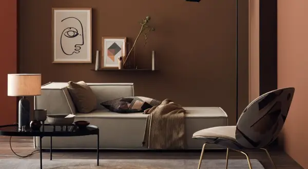 Gemütliches Wohnzimmer mit einer braunen Wand, einem hellen Sofa, einem auffälligen Sessel und einem Couchtisch.