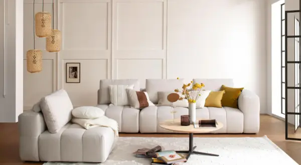 Gemütliches Wohnzimmer mit beiger Couch, Kissen, Couchtisch und Körblampen. Perfekt für slow living einrichtung.