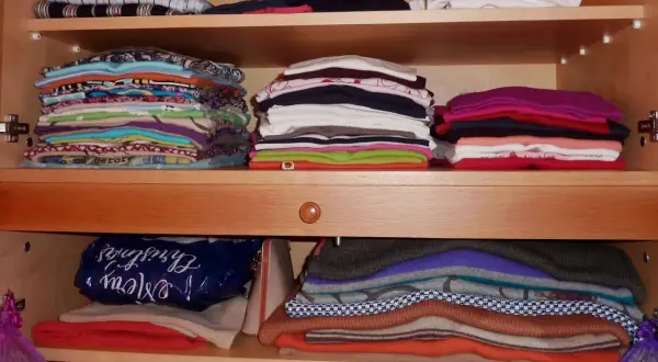 Ordentlich gestapelte Kleidung in einem Schrank. Zeit zum **Kleidung aussortieren** und Platz schaffen für Neues.