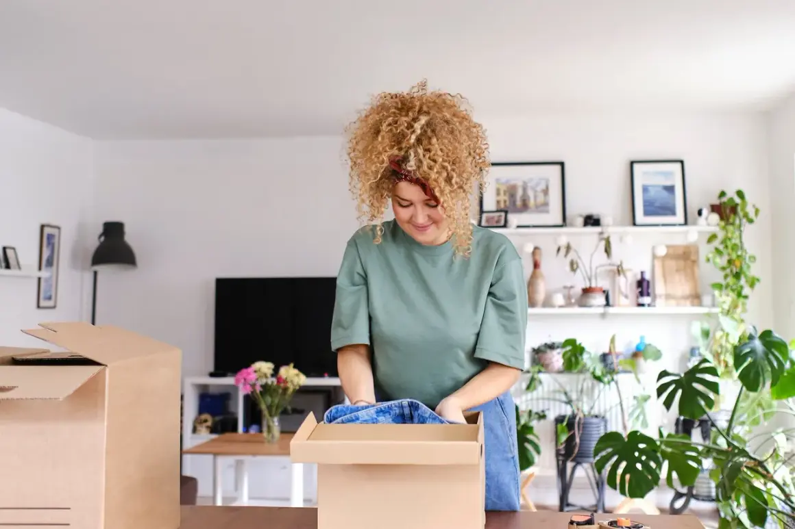 Frau packt Kleidung in einen Karton. Sie sortiert ihre Sachen, vielleicht für den Verkauf von Flohmarktartikeln.