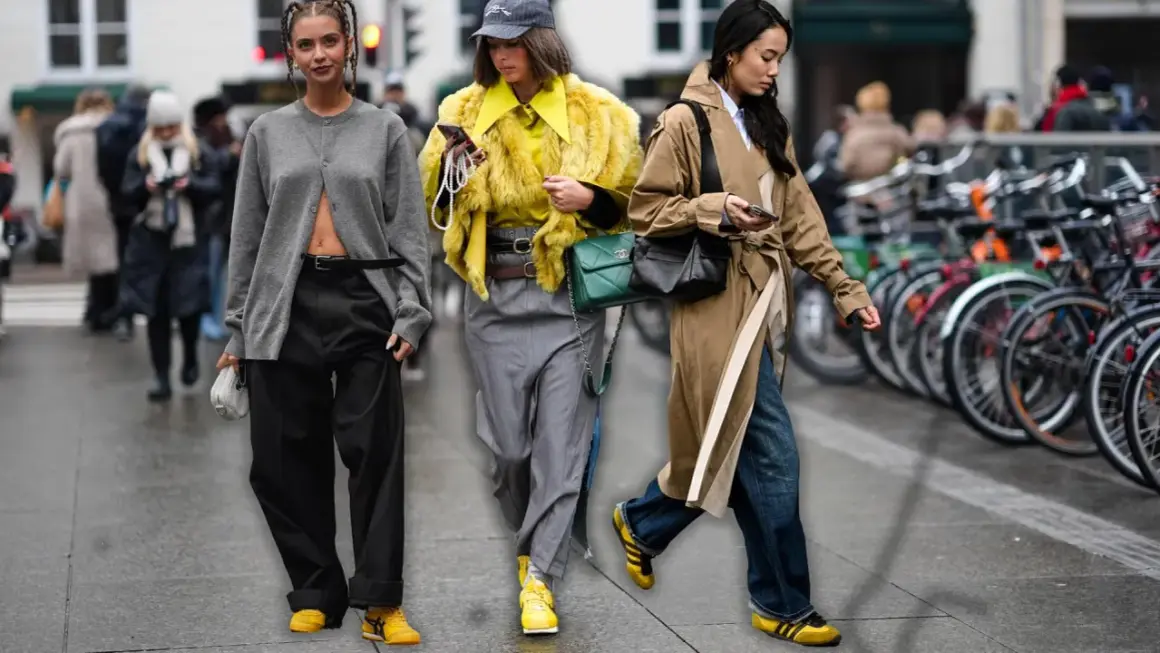 Drei Frauen in modischen Outfits, die die Herbstfarbe Gelb und Grau tragen, spazieren durch die Stadt.