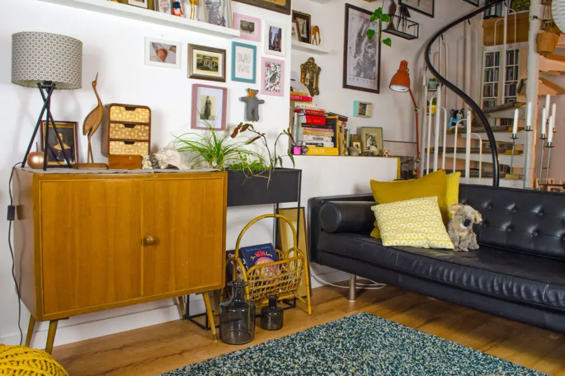 Gemütliche hygge einrichtung mit Vintage-Möbeln, Kunst und Pflanzen. Ein schwarzes Ledersofa lädt zum Entspannen ein.