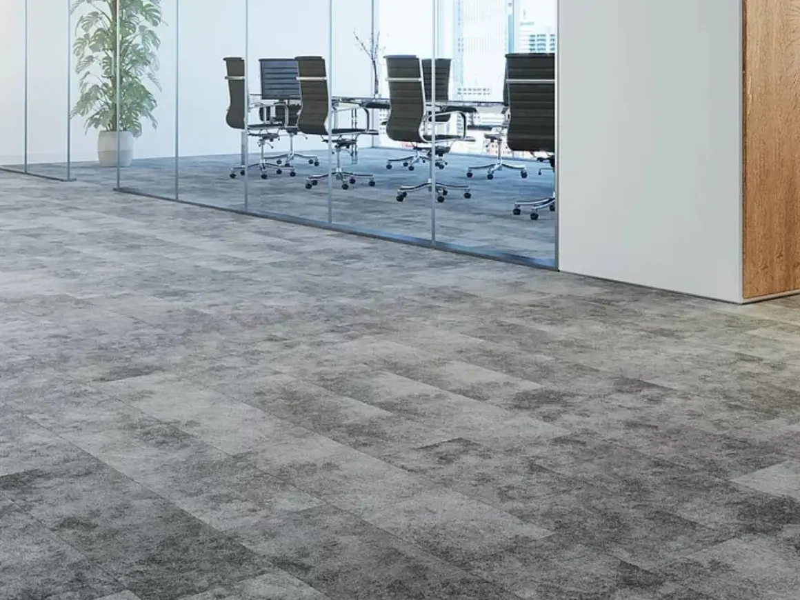 Moderner Teppichboden in Grau auf grauen Fliesen, der einen stilvollen Übergang zu einem Konferenzraum mit Glaswänden und Bürostühlen schafft.