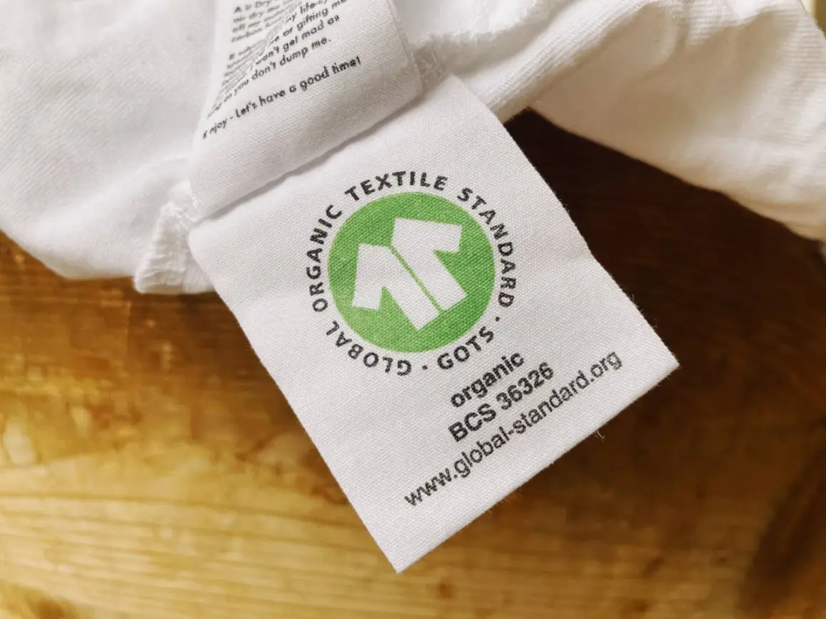 GOTS-zertifiziertes Textiletikett auf weißem Stoff. Die Kritik an der Textilindustrie wird durch das Siegel "Global Organic Textile Standard" entkräftet.