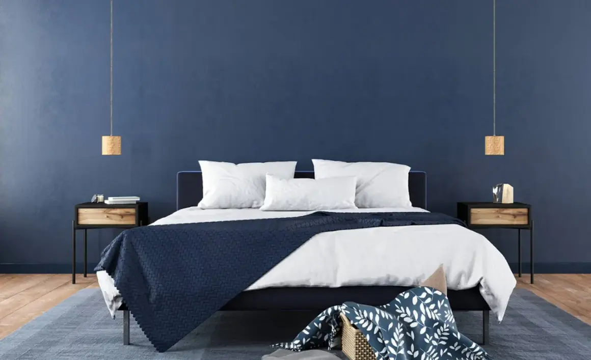 Ein modernes Schlafzimmer mit tiefblauen Wänden, die zum Streichen in Blau einladen. Ein dunkles Bett mit weißen Kissen und einer blauen Decke.